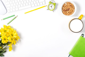 White keyboard, mouse, colorful stationery, yellow flowers, plate with granola and large cup of milk on white background. Concept of healthy lifestyle at office. Top view.