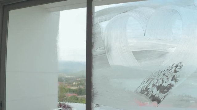 Funny man cleaner drawing heart on soap window glass during washing