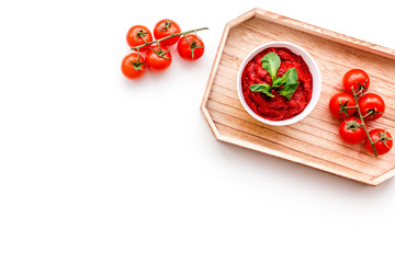 Tomato sauce in bowl with green basil near cherry tomatoes in wooden tray on white background top view copy space