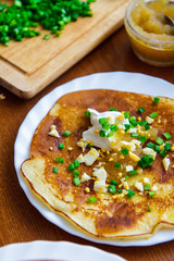 Pancake with sour cream and green onion on a white plate