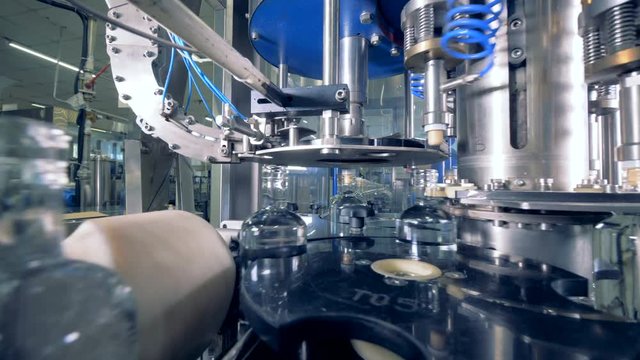 Full bottles move on a line, while factory equipment places corks. 4K.