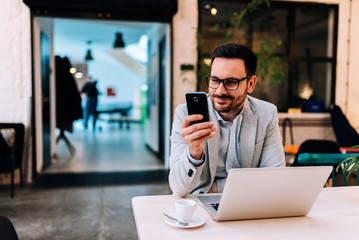 Portrait of smiling man looking at smartphone at the cafe.