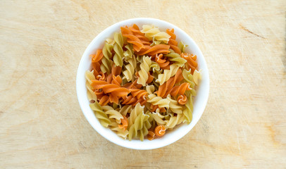 Multicolor spiral macaroni pasta in a white cup on a wooden table textured background, in the center with the top.