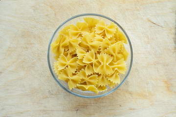 farfalle macaroni pasta in a glass bowl on a wooden table texture background, in the center with the top.