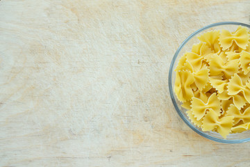 farfalle macaroni Pasta in a glass cup on a wooden table textured background with a side. Close-up with the top. With space for text.