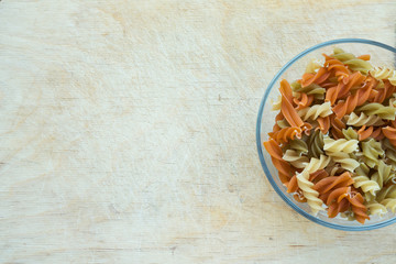 Multicolor spiral macaroni Pasta in a glass cup on a wooden table textured background with a side. Close-up with the top. With space for text.