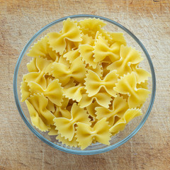 farfalle macaroni pasta in a glass bowl on a wooden cutting board, texture background, in the center close-up with the top.