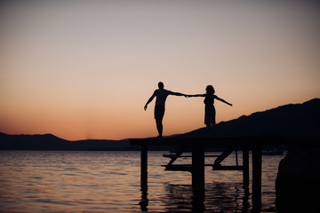 Couple in love on romantic date in evening at dock, copy space. Romance and love concept. Silhouette of sensual couple dancing on pier with sunset above sea surface on background.