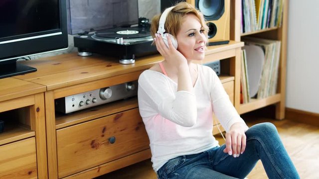 beautiful woman sitting next to a turntable with headphones on her head and listens to music