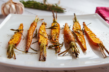 Roasted carrots with rosemary and spices on a white plate side view