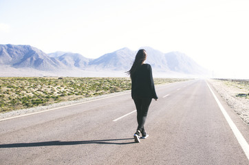 young woman with long hair walks alone on a long straight road