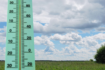 Street thermometer with a high temperature in the background of a sunny summer landscape.