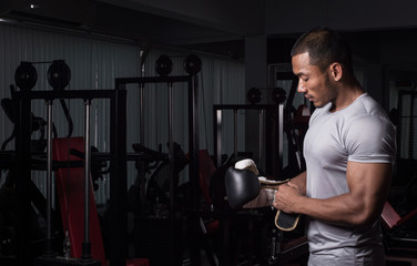 Muscular builder man with boxing gloves posing at fitness gym club