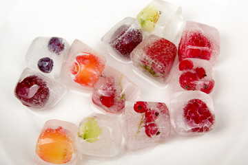 Berries frozen in ice cubes with mint on plate.