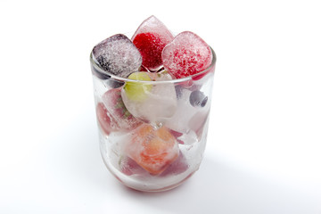 Berries frozen in ice cubes with mint in glass on wooden table background