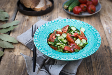 On a light blue plate a salad of fresh cucumbers and tomatoes with greens
