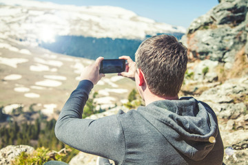travel guy sits on top of the mountain and takes pictures of the smartphone View from back of the tourist traveler on background mountain