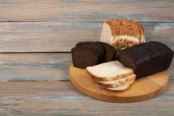 Many mixed breads and rolls of baked bread on wooden table background.