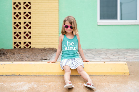 Girl wearing pink sunglasses and tank top sitting on curb