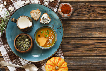 Close-up photo of  plate with fresh homemade pumpkin cream soup with seeds and heart shape toasts  on vintage wooden  background.