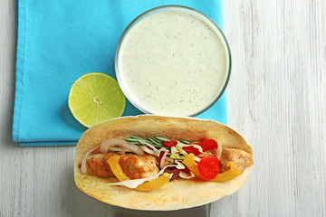 Tasty creamy lime sauce in bowl and fish taco on table