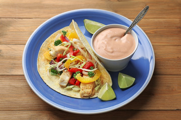 Plate with tasty creamy sauce in bowl and fish taco on wooden table
