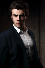 Obraz premium Sexy serious male business model posing in blue suit and white style shirt on dark shadow background. Fashion style contrast vogue portrait