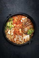 Traditional Korean kimchi jjigae with grilled pork belly and ramen as top view in a pot