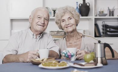 Smiling elderly spouses enjoying tea with sweets