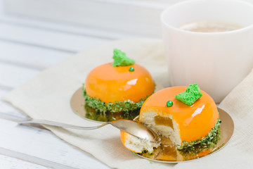 Tasty orange mousse cakes and cup of coffee on white wooden tray