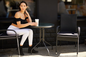 Brunette girl stand on the street look at camera and dring her delicious coffee from white cup, spring time photo shoot