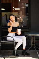 Obraz na płótnie Canvas Pretty girl sitting near coffee place and talk at her phone
