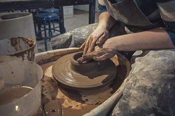 Craftsman woman potter in apron at work. Craftsman artist shapes the jug with his hands on pottery wheel