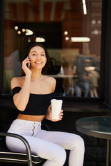 Pretty girl sitting near coffee place and talk at her phone