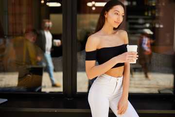 Brunette girl stand on the street look at camera and dring her delicious coffee from white cup, spring time photo shoot