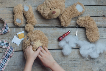 A girl sews a bear toy. Handicraft with children. Child fills the toy with a sintepon. - obrazy, fototapety, plakaty