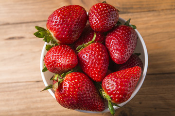 White bowl with some strawberries on a wooden table