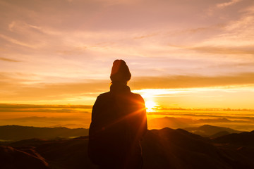 woman reaching the top of the mountain to see the golden sunset. 
