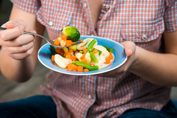 Girl with a plate of vegetables in hands. Healthy eating concept. Girl in jeans and a red shirt in a cage. Casual Style. Proper nutrition. Diet. Health. Vegetarian food. Vegans food.