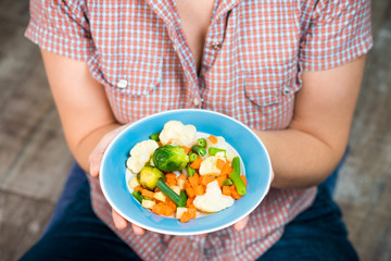 Girl with a plate of vegetables in hands. Healthy eating concept. Girl in jeans and a red shirt in a cage. Casual Style. Proper nutrition. Diet. Health. Vegetarian food. Vegans food.