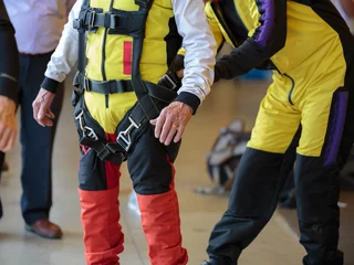 Foto auf Acrylglas Luftsport Fallschirmspringer-Ausbilder hilft Lehrling, den Sicherheitsgurt an seinem Fallschirmspringeranzug zu binden