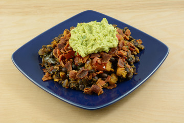 Party appetizer made from sweet potatoes, black beans, bacon and guacamole on blue plate
