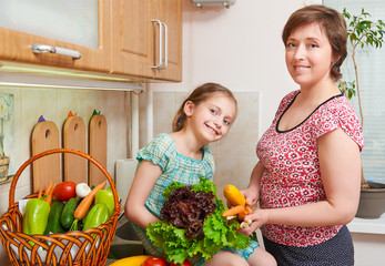Mother and daughter with basket of vegetables and fresh fruits in home kitchen interior - healthy food concept