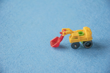 Small decorative toy excavator on blue background. Macro abstract photo. Construction, mining, construction equipment at work