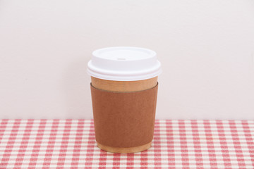 Cardboard throwaway coffee cup on red and white checkered table 