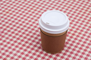 Cardboard throwaway coffee cup on red and white checkered table 