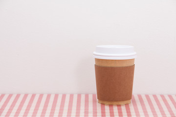 Cardboard throwaway coffee cup on red and white checkered table 