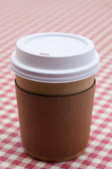 Cardboard throwaway coffee cup on red and white checkered table 