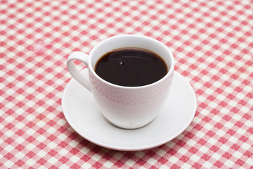 A cup of coffee on red and white checkered table 