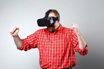 Portrait of bearded man watching virtual reality glasses over gray background with copyspace.